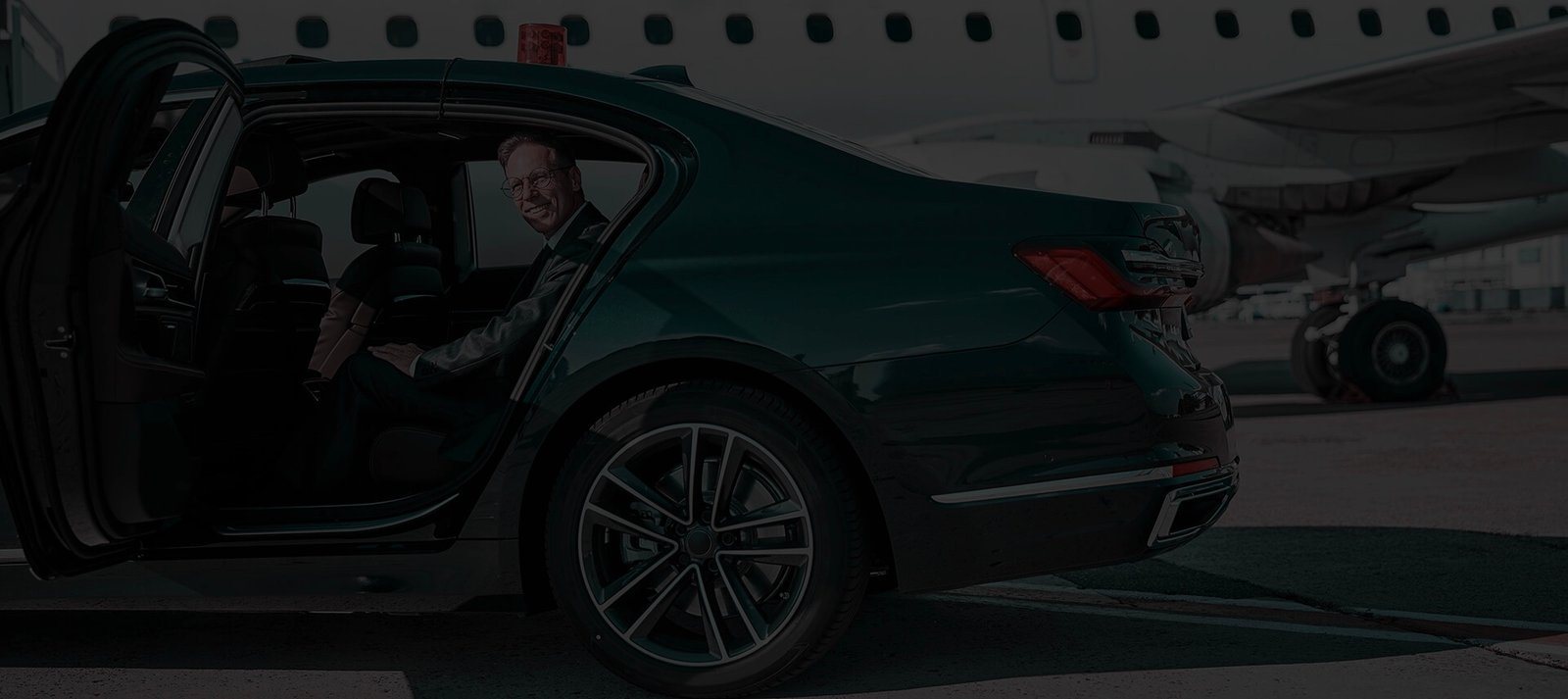 A chauffeur opening the rear door for a passenger beside a private jet
